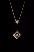Gold necklace with a square pendant featuring intricate designs and blue gemstones, set against a black background.
