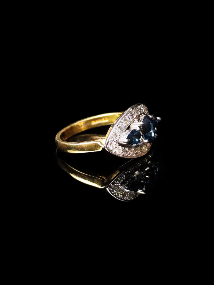 18ct Gold Three-Stone Sapphire Ring with a Diamond Halo, showcased against a black background.