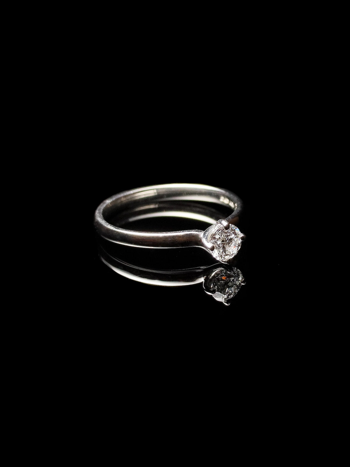 A solitaire ring featuring a round brilliant diamond set in platinum with a twist design, displayed on a reflective black surface.