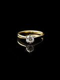 The 18ct Yellow Gold Round Brilliant 0.70ct Diamond Solitaire Ring is set against a black background, highlighting its reflective surface beneath.