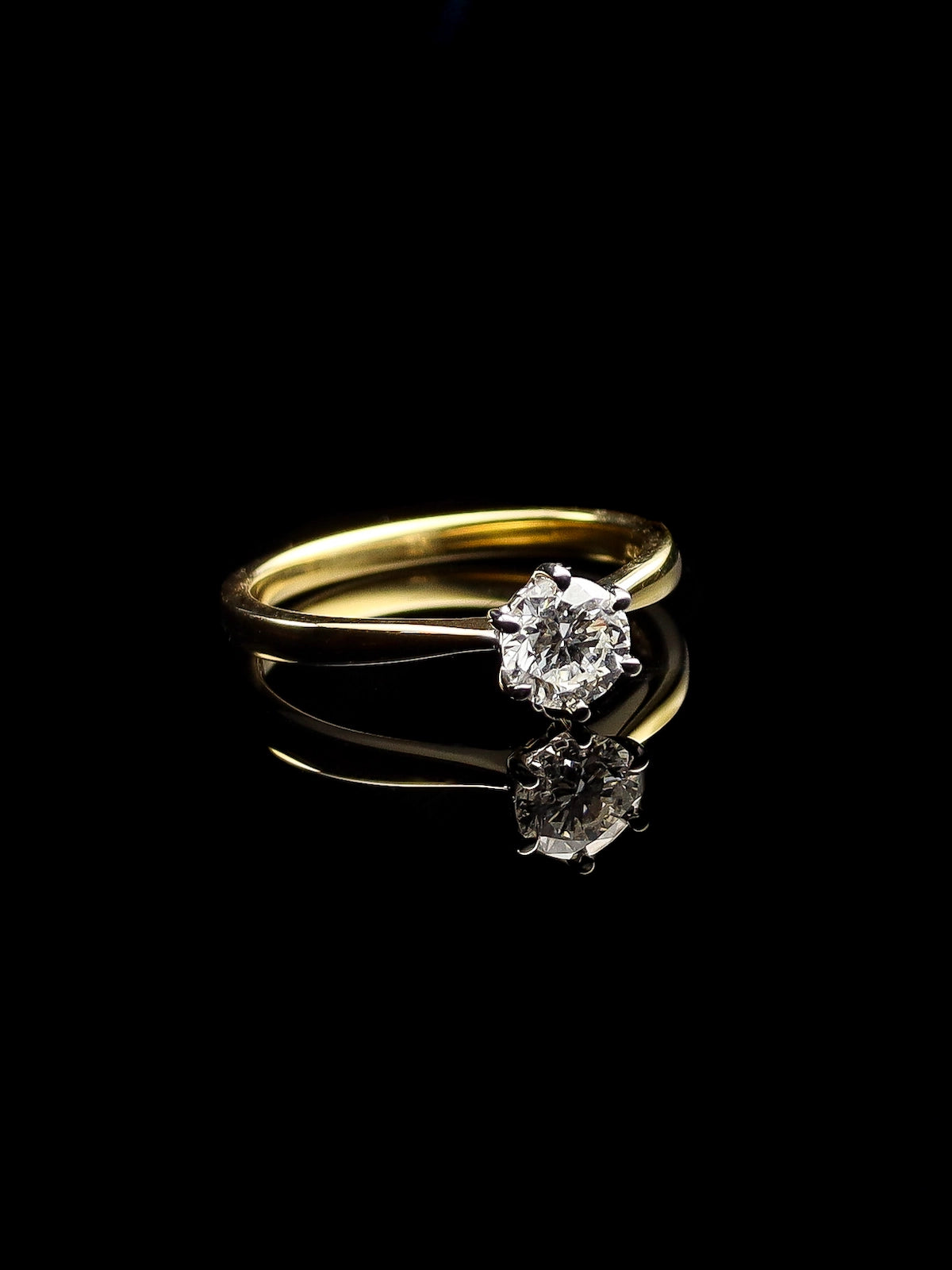 The 18ct Yellow Gold Round Brilliant 0.70ct Diamond Solitaire Ring is elegantly positioned on a reflective black surface.