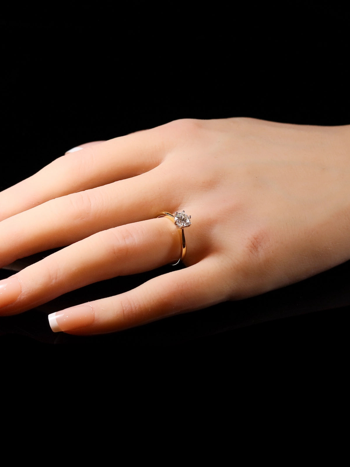 A hand wearing the 18ct Yellow Gold Round Brilliant 0.70ct Diamond Solitaire Ring on a dark background.
