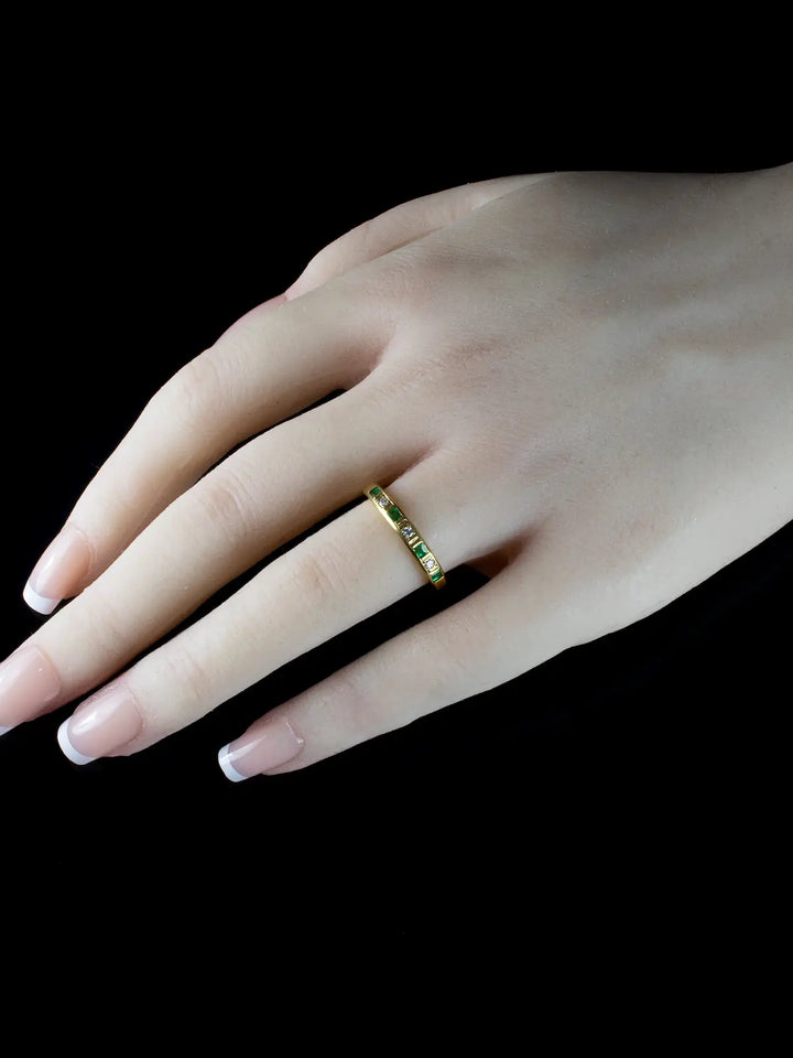 A hand adorned with a Vintage 18ct Gold Emerald and Diamond Half Eternity Ring is extended against a black background.