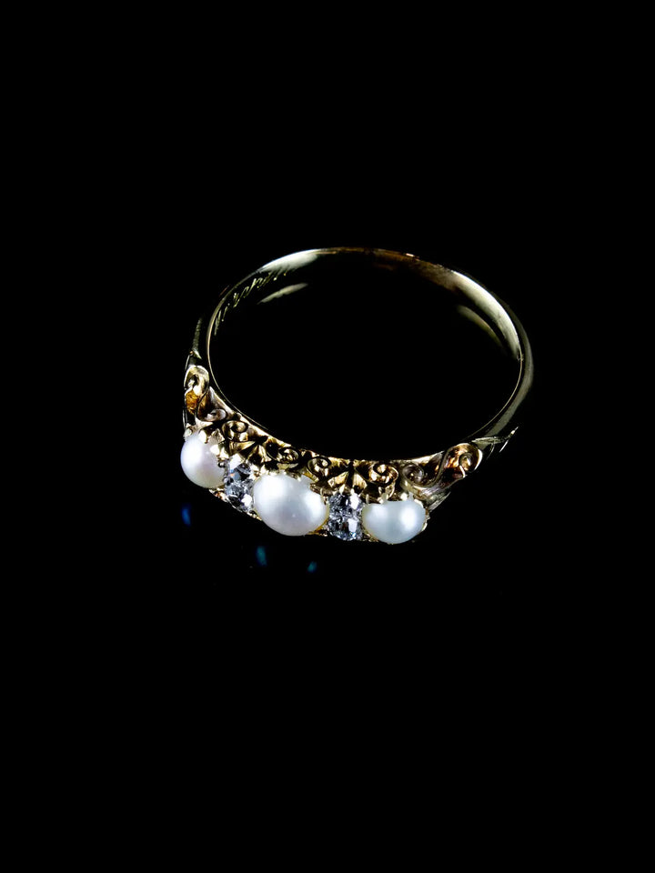 An Antique Victorian gold ring, circa 1880, featuring three pearls and small clear gemstones on a black background.