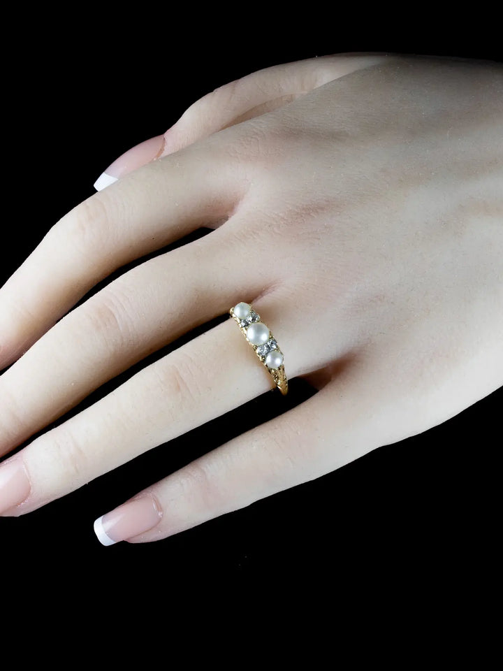 A hand with manicured nails is adorned with the Antique Victorian Seven Stone Pearl and Diamond Ring, Circa 1880, showcased against a black background.