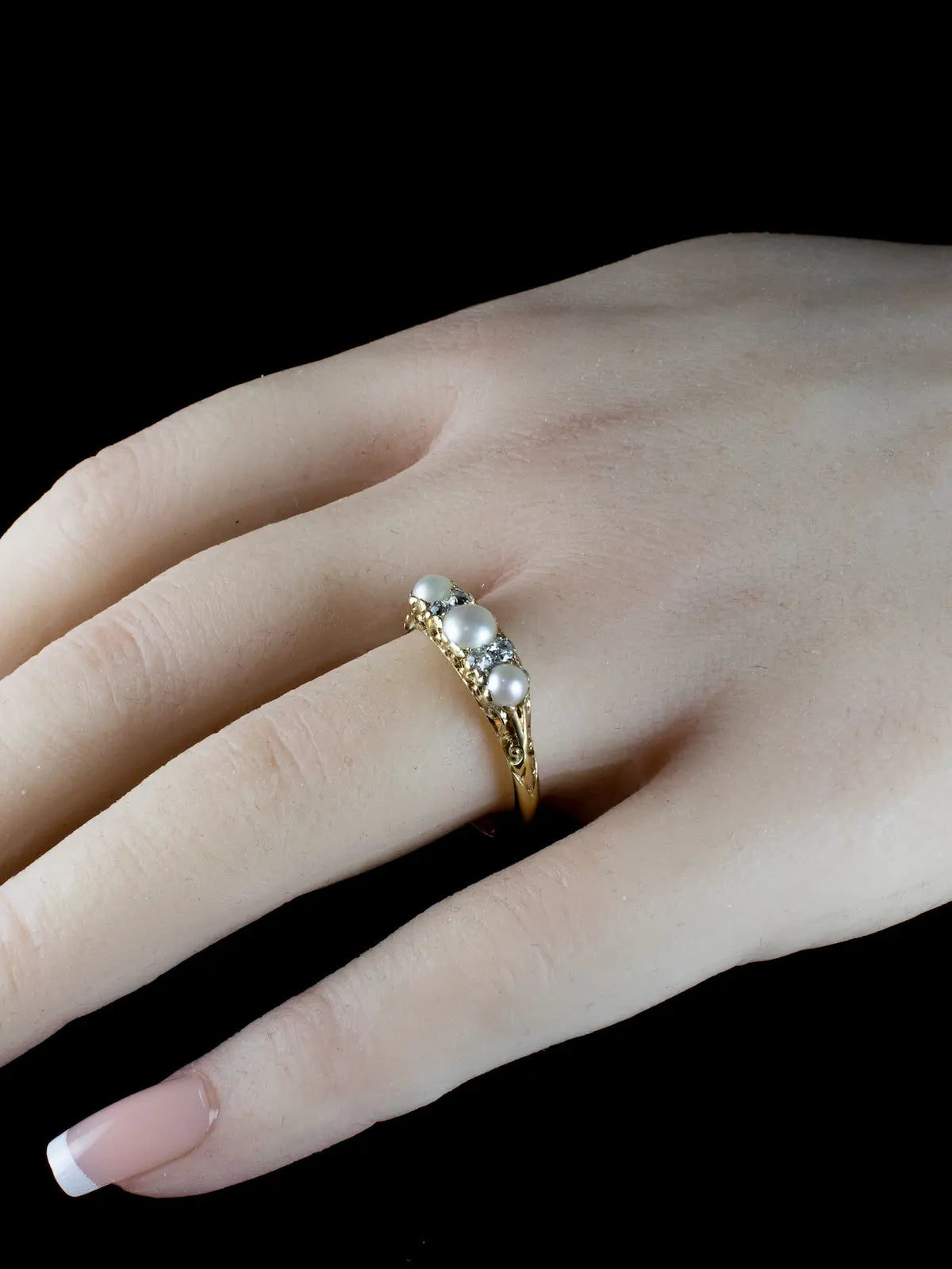 A hand showcasing an exquisite vintage ring, featuring seven pearls and dazzling diamonds from the Antique Victorian era, dating back to circa 1880.
