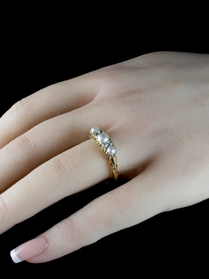 A hand showcasing an exquisite vintage ring, featuring seven pearls and dazzling diamonds from the Antique Victorian era, dating back to circa 1880.
