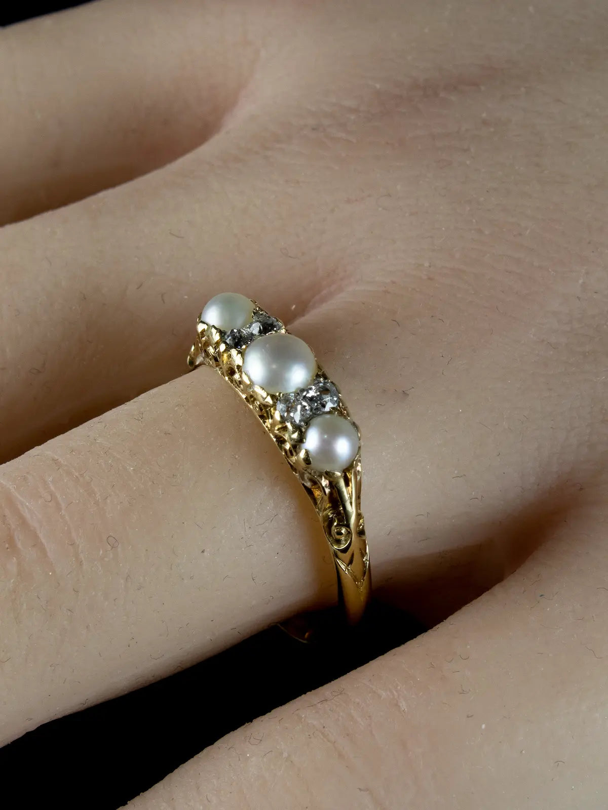 An Antique Victorian Seven Stone Pearl and Diamond Ring from circa 1880, featuring three pearls and small diamonds, is worn on a finger.