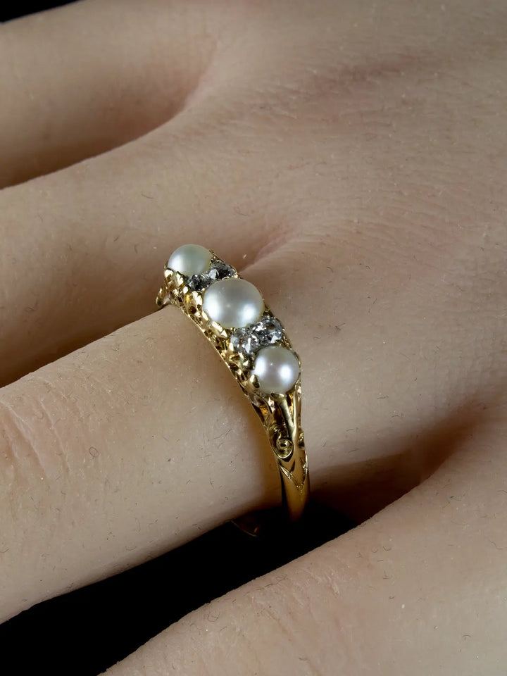 An Antique Victorian Seven Stone Pearl and Diamond Ring from circa 1880, featuring three pearls and small diamonds, is worn on a finger.