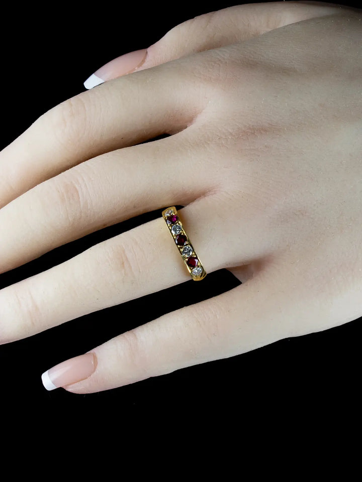 A hand adorned with an 18ct Gold Seven Stone Ruby and Diamond Half Eternity Ring on the ring finger is set against a black background.