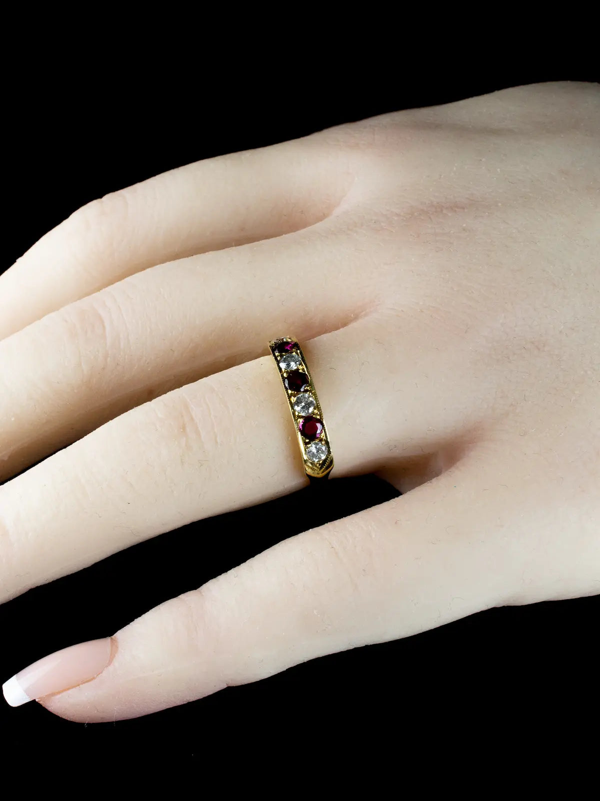 An 18ct gold ring with seven stones, including rubies and diamonds, is worn on a person's finger.