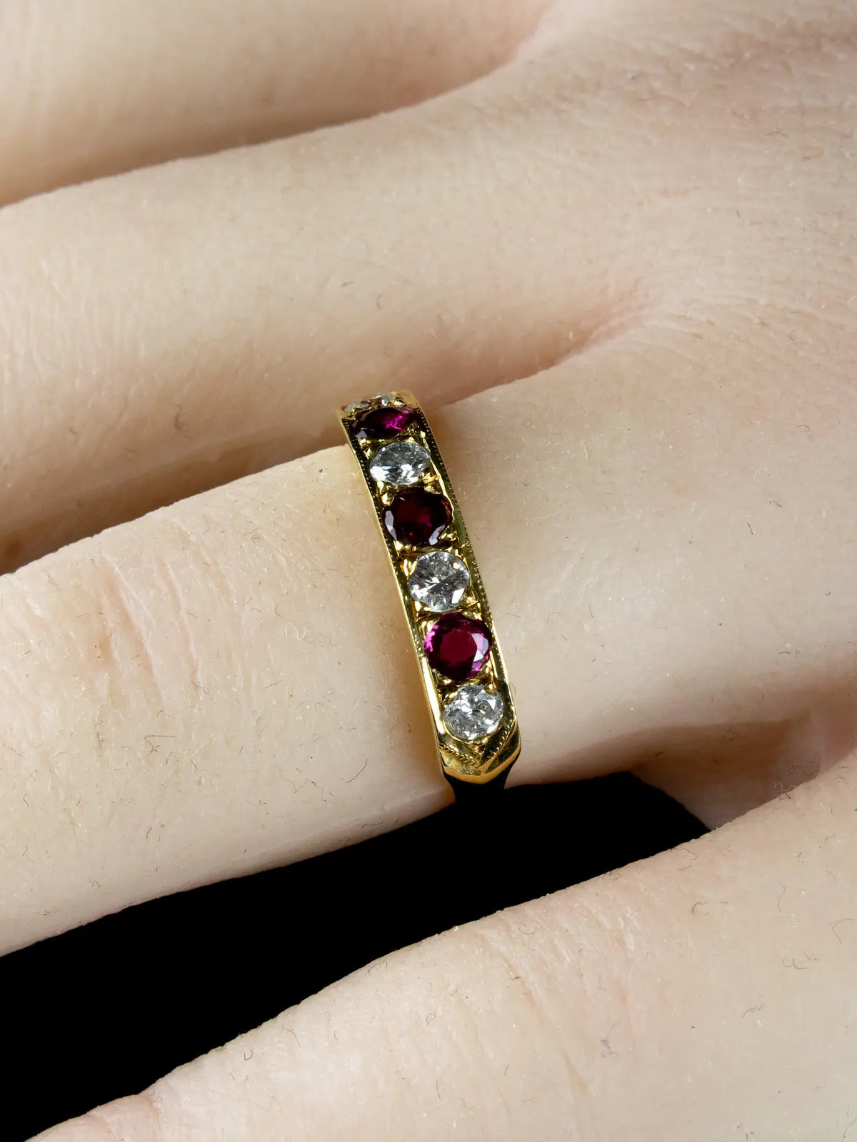 A finger adorned with an 18ct gold seven stone ruby and diamond half eternity ring.