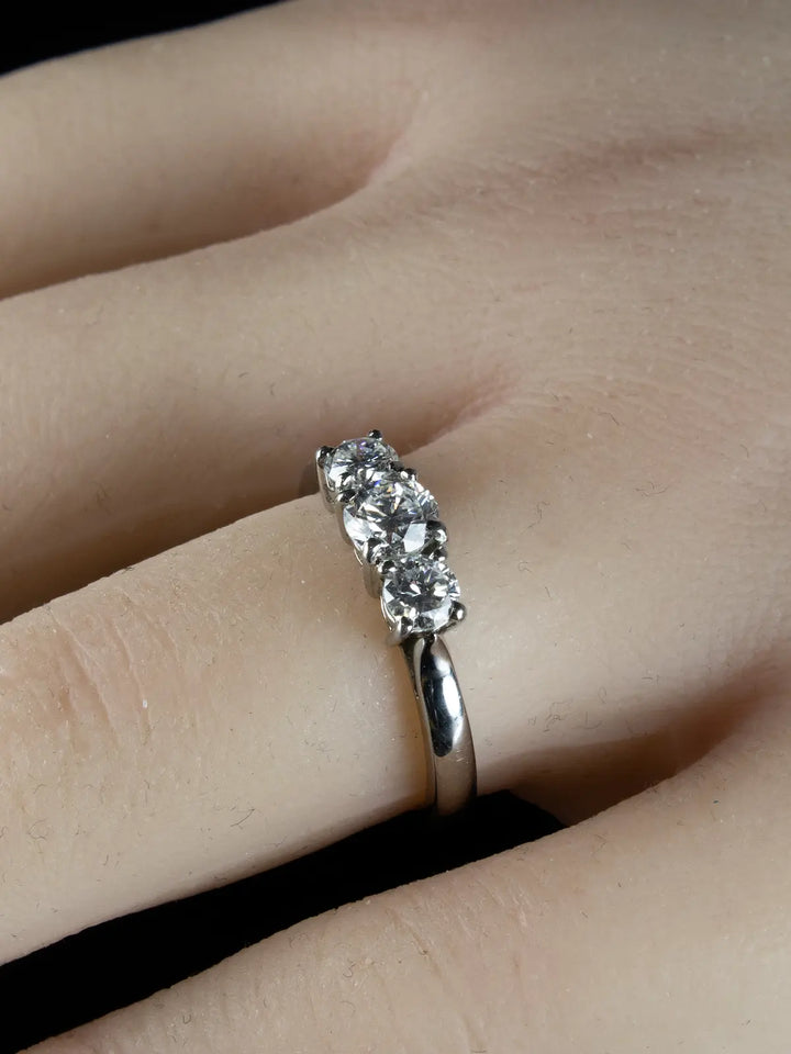 A Platinum Three Stone 0.92ct Diamond Ring is showcased on a finger against a dark background.